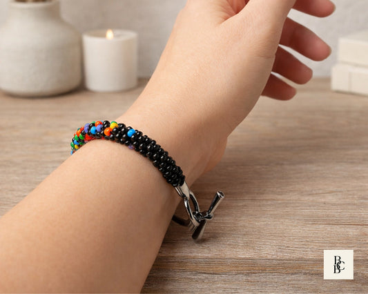 Confetti Explosion One Spectrum Pride Kumihimo bracelet worn on the wrist, showing multicolor glass seed beadwork with glossy black accents