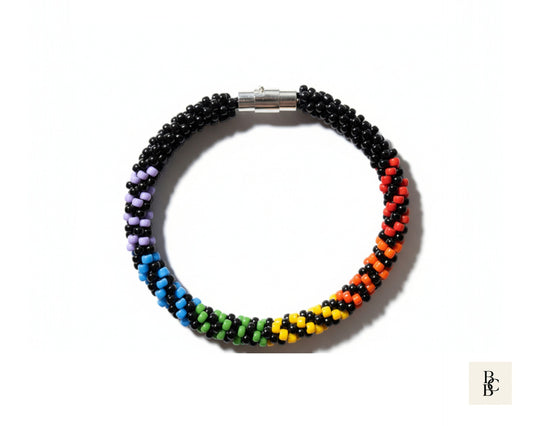 Overhead view of the Rainbow Illusion Pride Kumihimo bracelet with black and rainbow glass seed beads and a silver magnetic clasp.