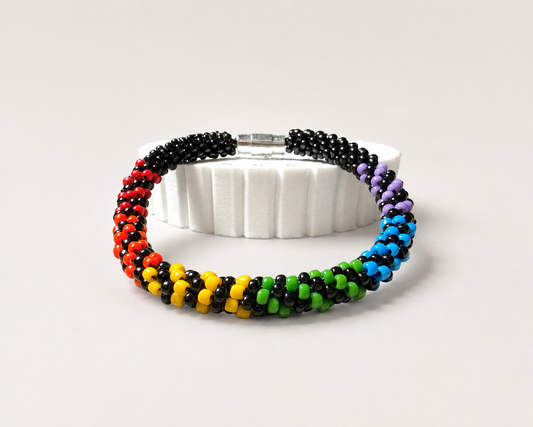 Rainbow Illusion Pride Kumihimo bracelet with black and rainbow glass seed beads, displayed on a white stand with a silver clasp.