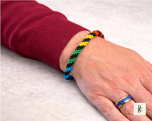 Rainbow Helix Kumihimo bracelet worn on the wrist, showing vivid rainbow spiral beadwork against glossy black seed beads.
