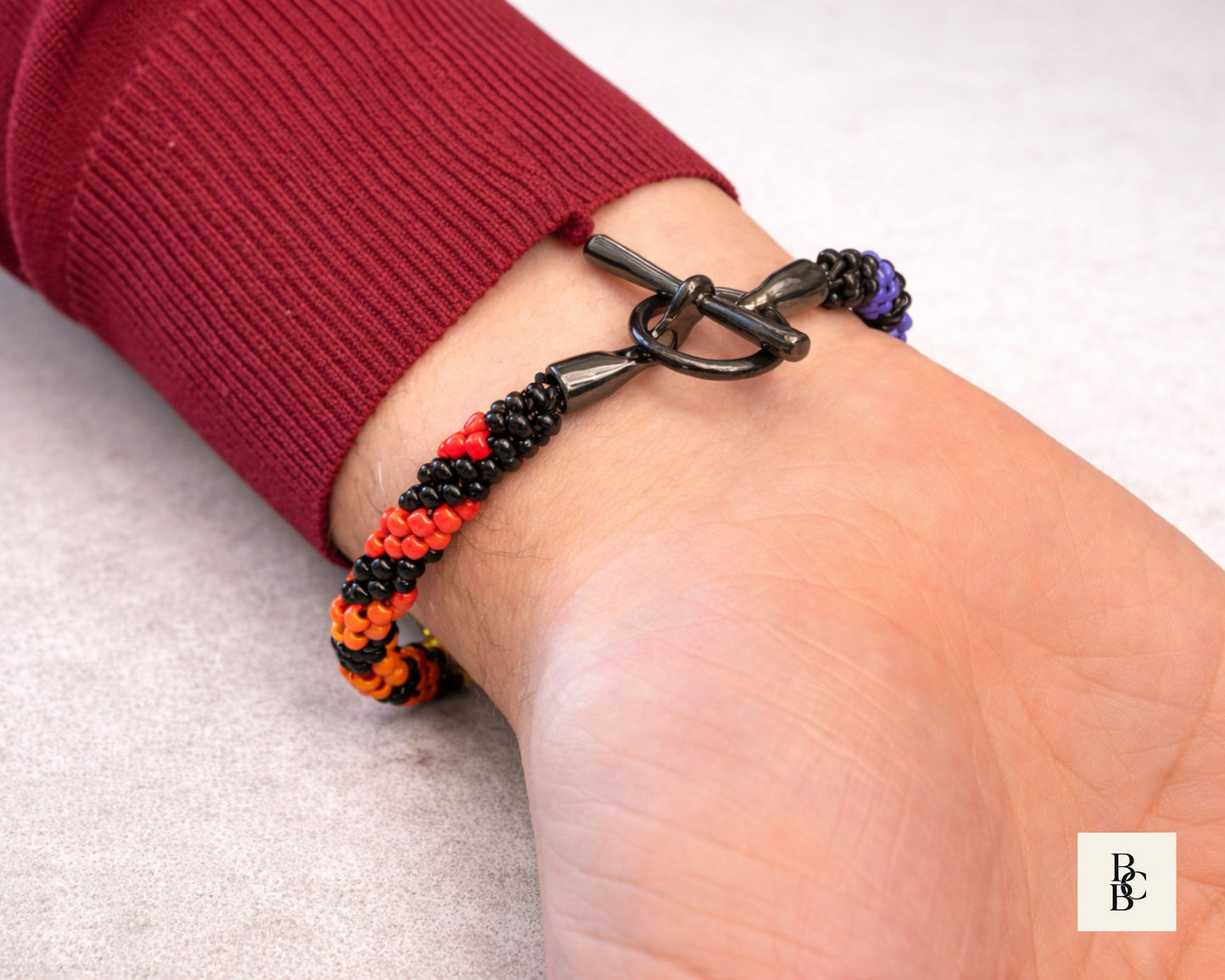 Close-up of the Rainbow Helix Kumihimo bracelet showing the gunmetal-tone toggle clasp and red, orange, and purple spiral beadwork.