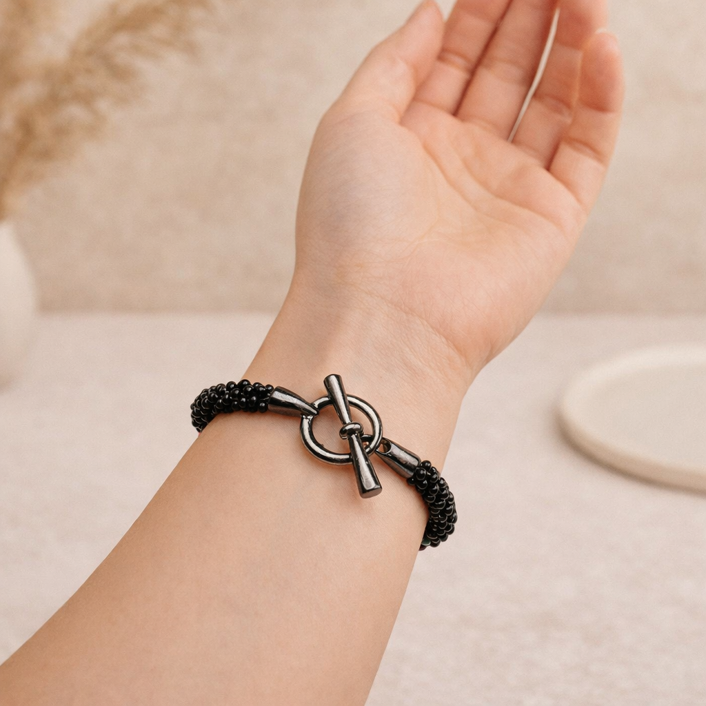 Close-up of the Rainbow Illusion Kumihimo bracelet on the wrist, showing the glossy black beadwork and gunmetal-tone toggle clasp.