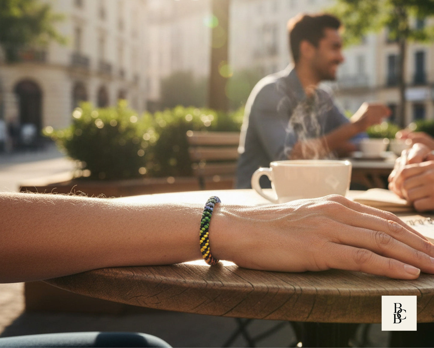 Rainbow Illusion Kumihimo bracelet worn at a sunlit outdoor café, featuring black glass seed beads with vivid rainbow accents.