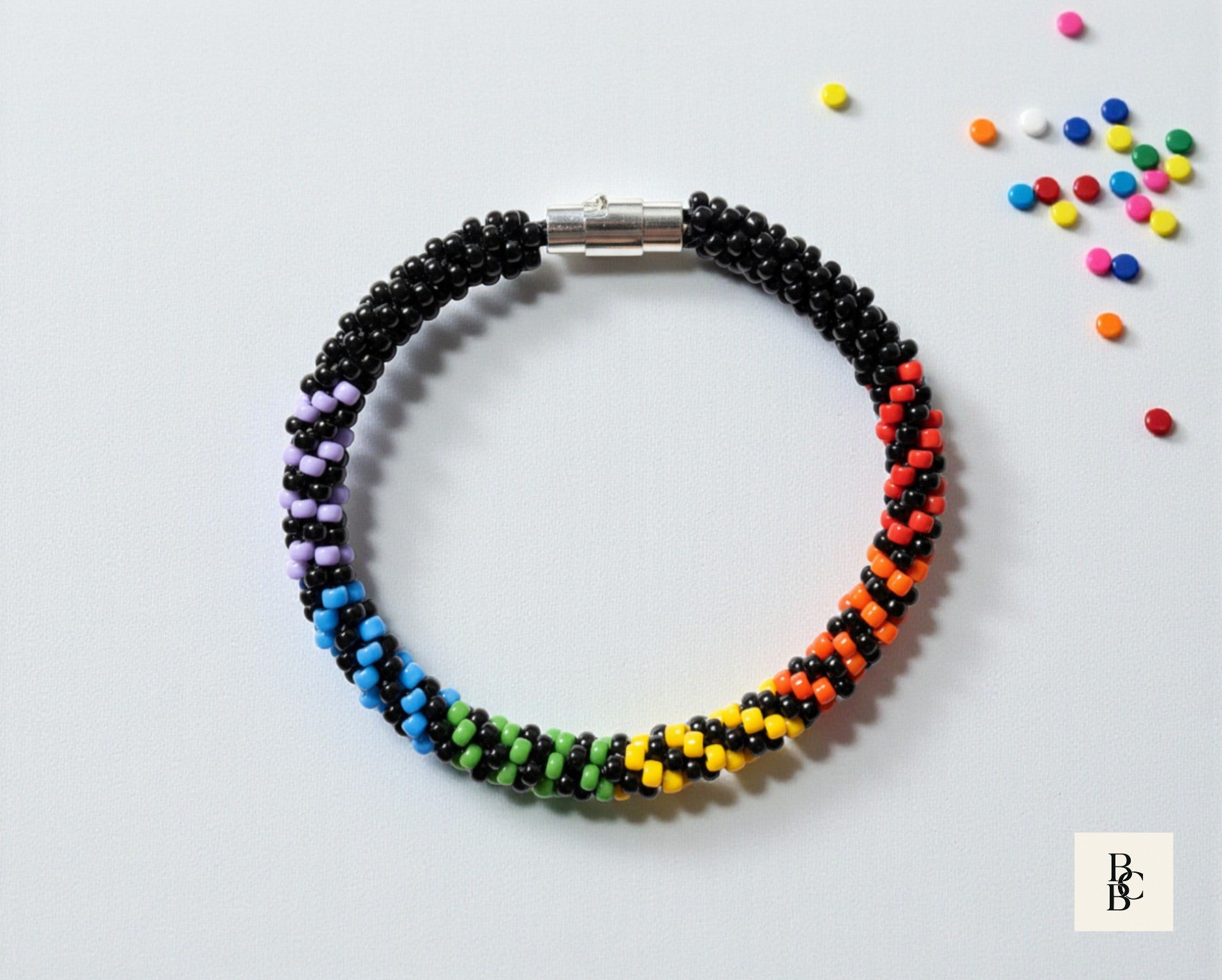 Flat lay of the Rainbow Illusion Pride Kumihimo bracelet with black and rainbow glass seed beads, silver clasp, and colorful bead accents.
